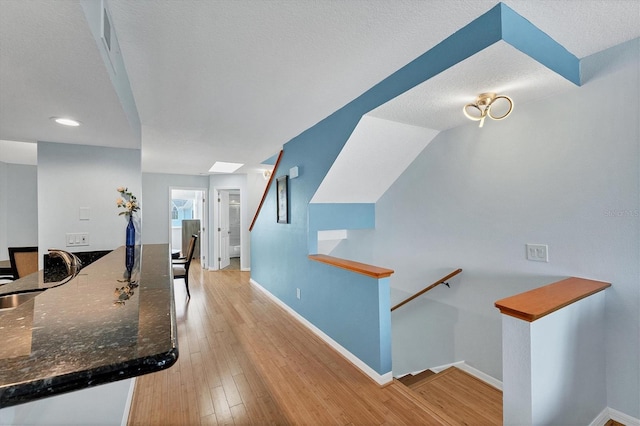 hall featuring a textured ceiling, a skylight, light hardwood / wood-style flooring, and sink