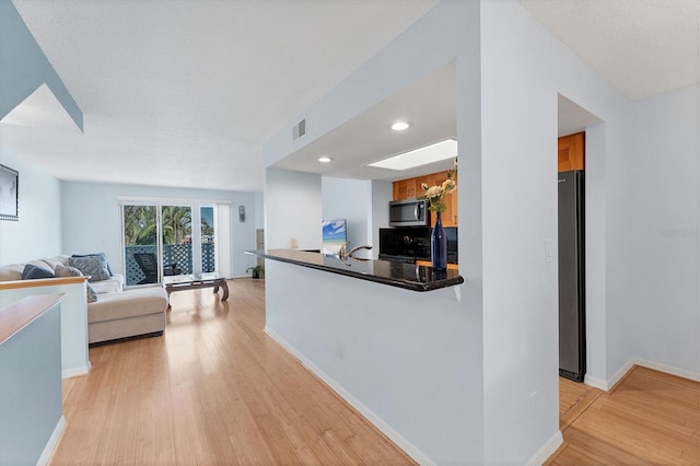 kitchen with kitchen peninsula, appliances with stainless steel finishes, and light wood-type flooring