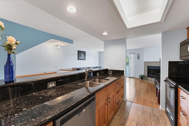 kitchen with dishwasher, black range with electric stovetop, sink, light wood-type flooring, and a fireplace