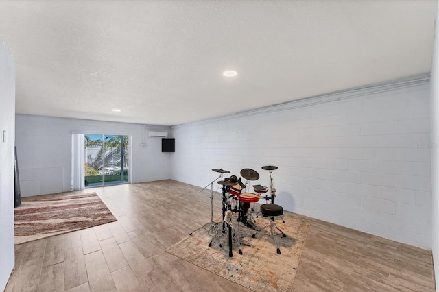 game room featuring light hardwood / wood-style floors, a textured ceiling, and a wall mounted AC