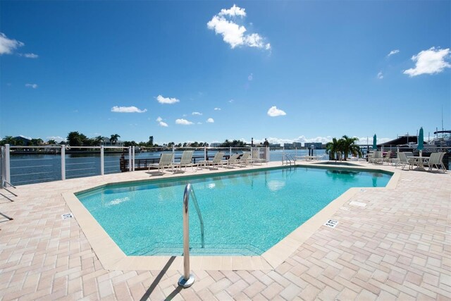 community pool with a patio area, a water view, and fence