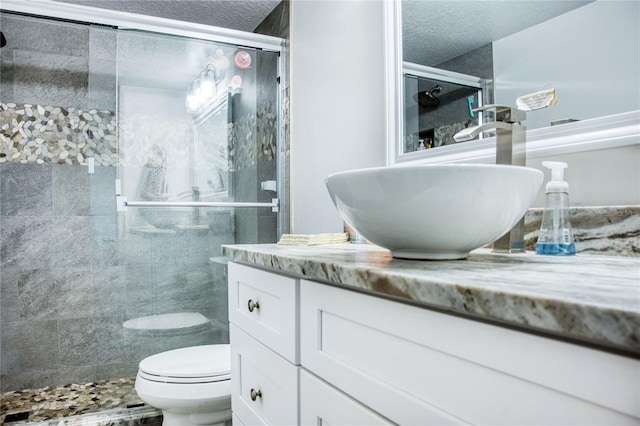 full bath featuring a stall shower, a textured ceiling, toilet, and vanity