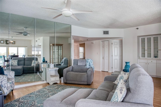 living room with ceiling fan, a textured ceiling, visible vents, and wood finished floors