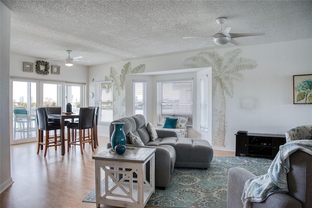 living room with light wood-style flooring, a textured ceiling, baseboards, and a ceiling fan