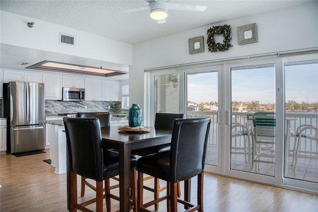 dining space featuring a ceiling fan, visible vents, a textured ceiling, and light wood finished floors