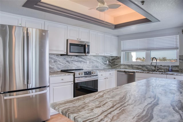 kitchen with appliances with stainless steel finishes, a tray ceiling, white cabinets, and light stone counters