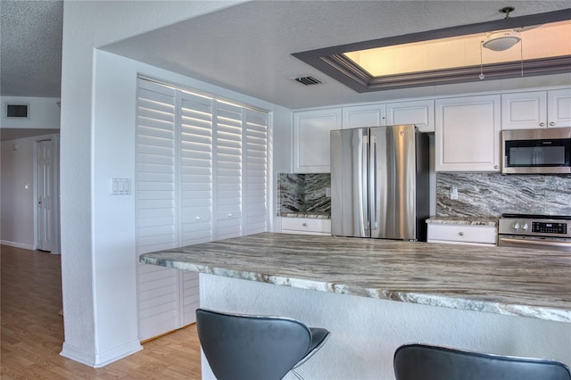 kitchen featuring a textured ceiling, light wood-style flooring, white cabinets, appliances with stainless steel finishes, and tasteful backsplash