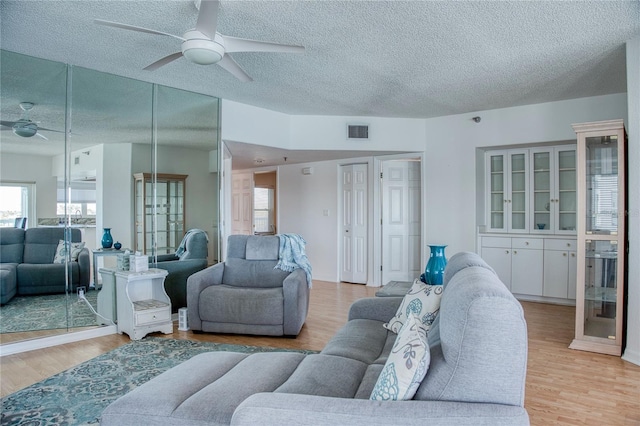 living room featuring a ceiling fan, visible vents, a textured ceiling, and light wood finished floors