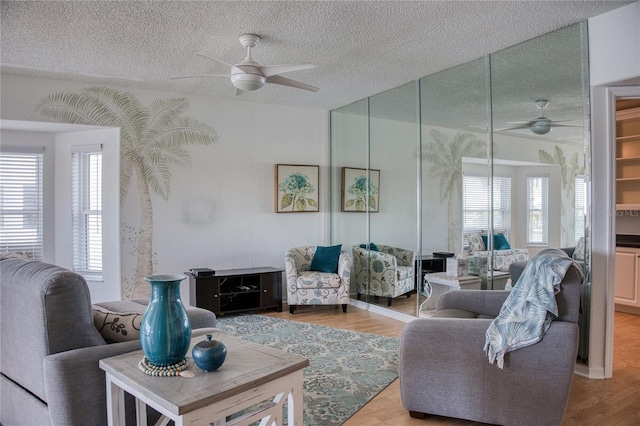 living room featuring ceiling fan, light wood-style flooring, and a textured ceiling