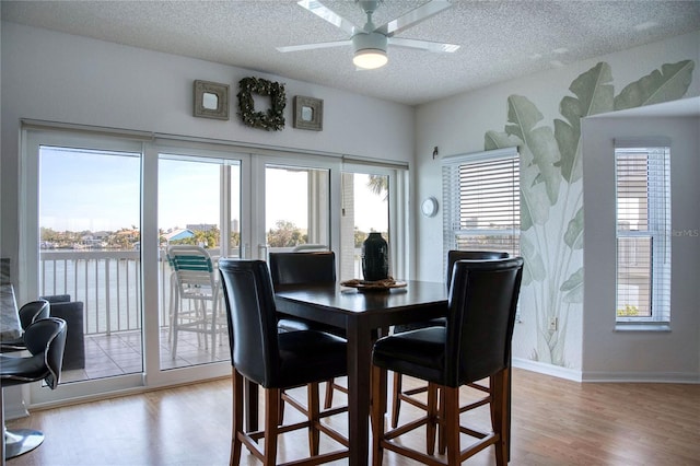 dining space with a textured ceiling, light wood-type flooring, french doors, and a water view