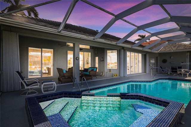 pool at dusk with glass enclosure and a patio area