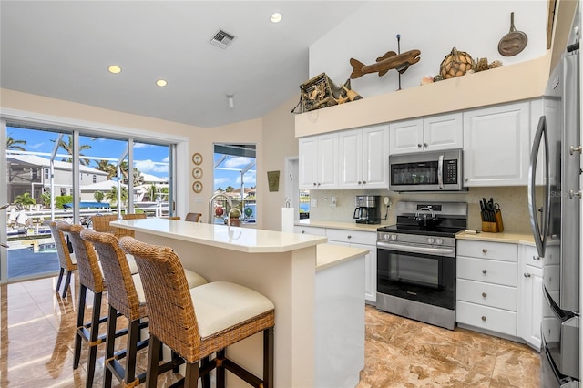 kitchen with decorative backsplash, stainless steel appliances, white cabinetry, a breakfast bar area, and an island with sink