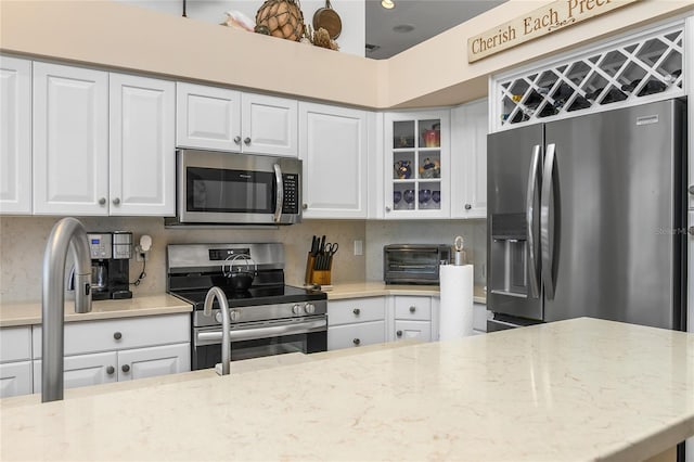 kitchen with decorative backsplash, white cabinets, light stone counters, and appliances with stainless steel finishes