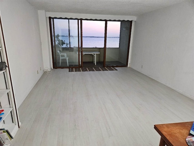 empty room featuring a water view, a textured ceiling, and wood finished floors