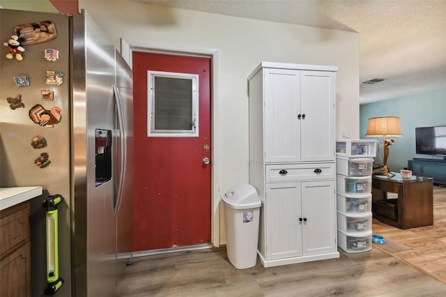 kitchen with stainless steel fridge with ice dispenser, a textured ceiling, light hardwood / wood-style floors, and white cabinetry