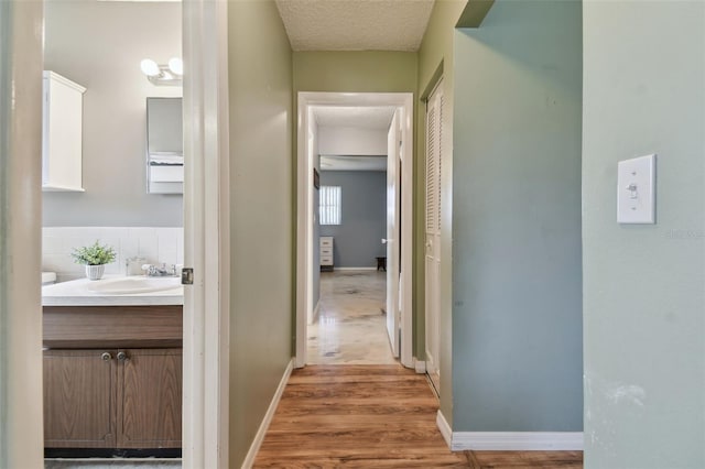 hall with a textured ceiling, sink, and light hardwood / wood-style flooring