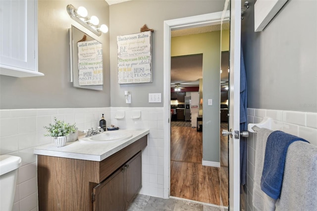 bathroom featuring vanity, hardwood / wood-style flooring, ceiling fan, toilet, and tile walls