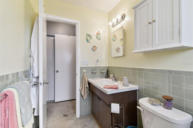 bathroom with a textured ceiling, vanity, toilet, and tile walls