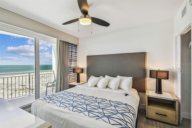 bedroom with access to outside, a water view, dark hardwood / wood-style floors, ceiling fan, and a beach view