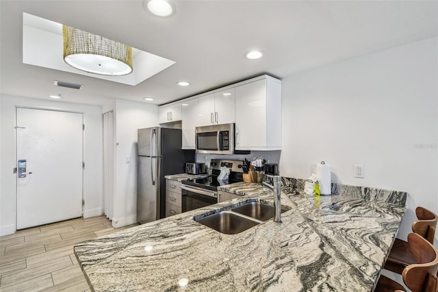 kitchen featuring kitchen peninsula, stainless steel appliances, white cabinetry, and sink