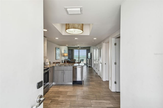 kitchen featuring hardwood / wood-style floors, ceiling fan, a tray ceiling, kitchen peninsula, and stainless steel appliances