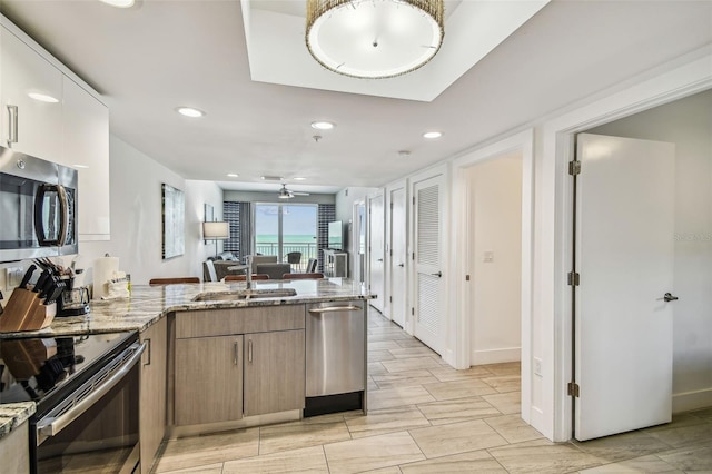 kitchen with sink, ceiling fan, appliances with stainless steel finishes, light stone counters, and kitchen peninsula