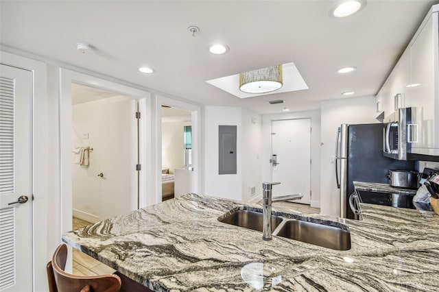 kitchen with light stone counters, stainless steel appliances, sink, white cabinets, and electric panel