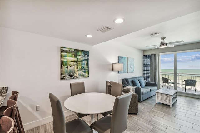 dining space with ceiling fan, a water view, and light hardwood / wood-style floors