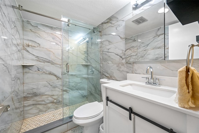 bathroom with a textured ceiling, vanity, tile walls, toilet, and a shower with shower door