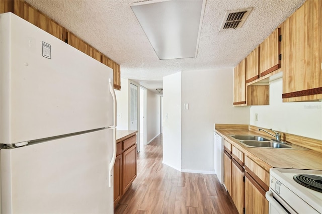 kitchen with a textured ceiling, light hardwood / wood-style floors, white appliances, and sink