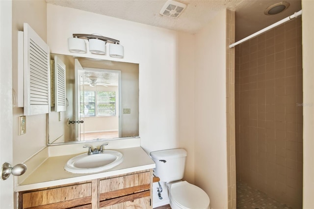 bathroom with a tile shower, vanity, a textured ceiling, and toilet