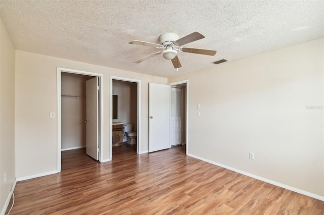 unfurnished bedroom with connected bathroom, ceiling fan, a spacious closet, a textured ceiling, and hardwood / wood-style flooring