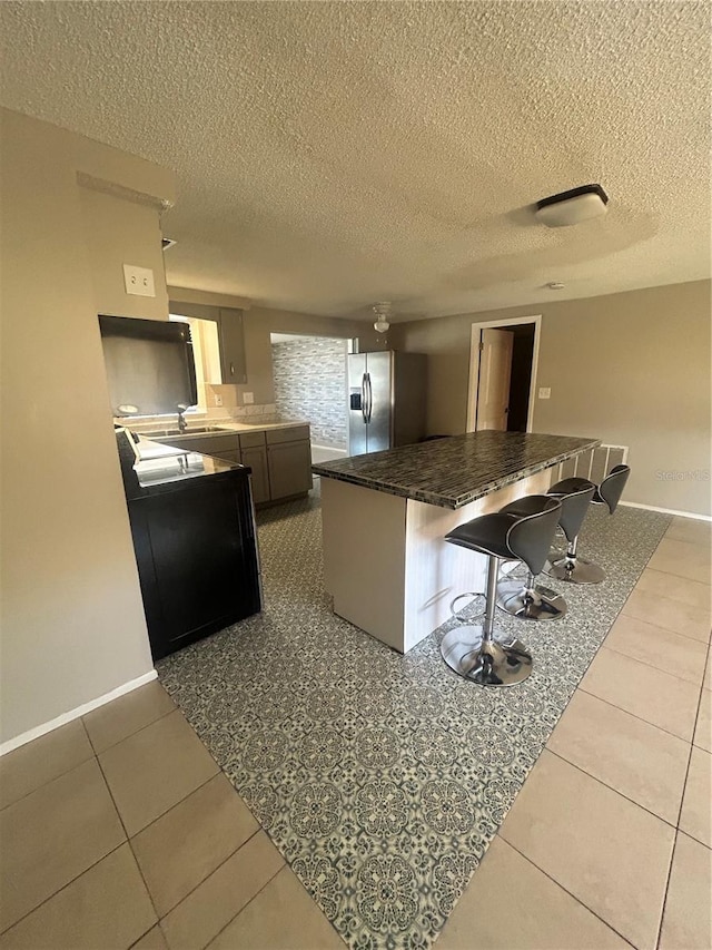 kitchen featuring a breakfast bar, stainless steel fridge with ice dispenser, a textured ceiling, and light tile patterned flooring