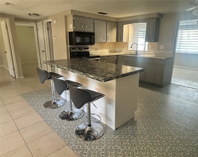 kitchen featuring a breakfast bar area, gray cabinetry, electric range, and sink