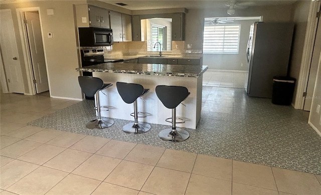 kitchen with ceiling fan, sink, stainless steel appliances, a kitchen breakfast bar, and light tile patterned floors