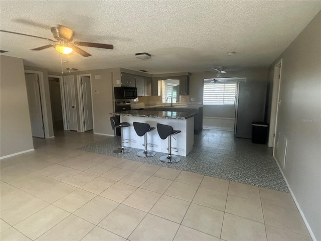 kitchen with stainless steel range with electric stovetop, light tile patterned flooring, a kitchen bar, and a textured ceiling