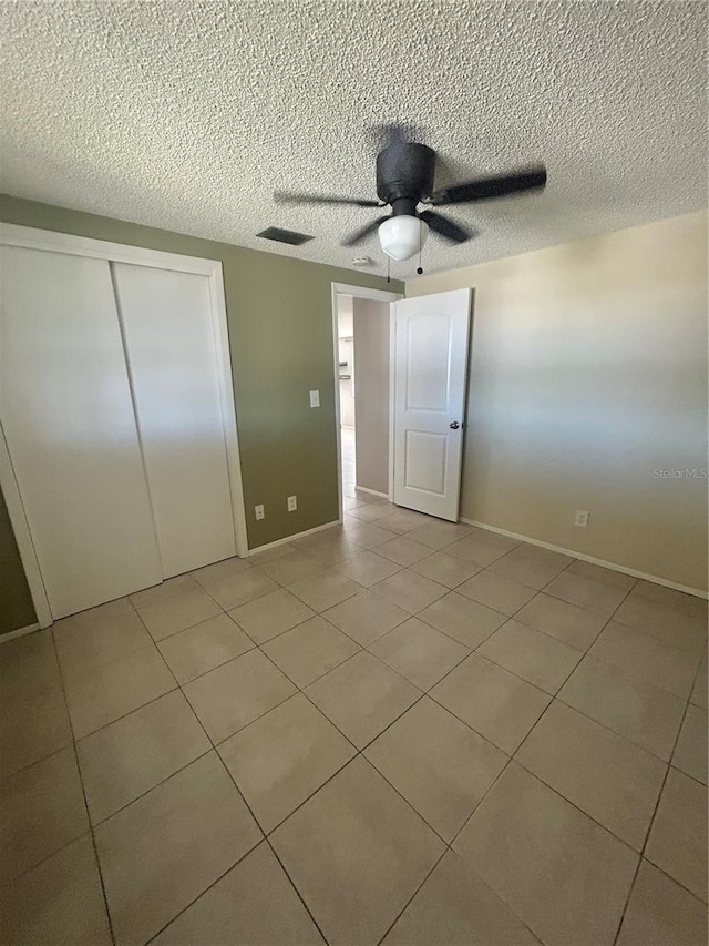 unfurnished bedroom with ceiling fan, a closet, light tile patterned floors, and a textured ceiling