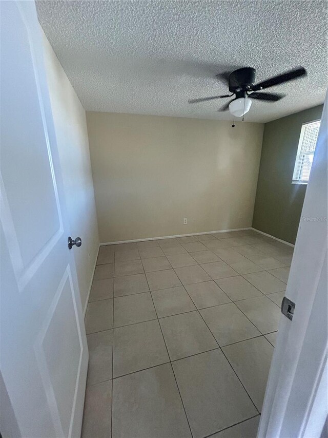 unfurnished room featuring ceiling fan, light tile patterned floors, and a textured ceiling