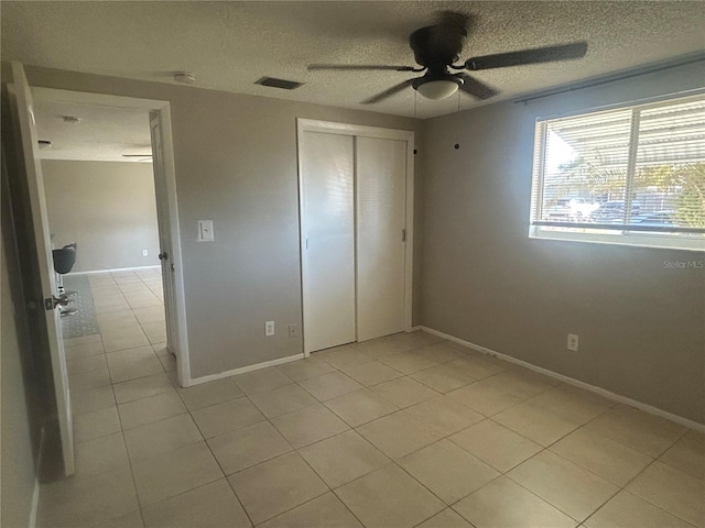 unfurnished bedroom featuring ceiling fan, light tile patterned flooring, a textured ceiling, and a closet