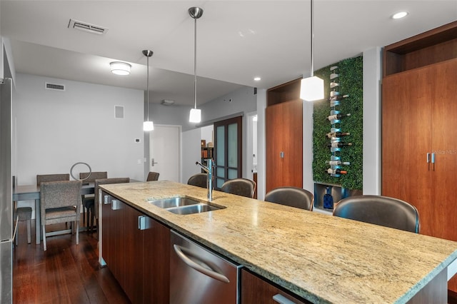 kitchen featuring dark hardwood / wood-style flooring, light stone counters, stainless steel dishwasher, sink, and a center island with sink