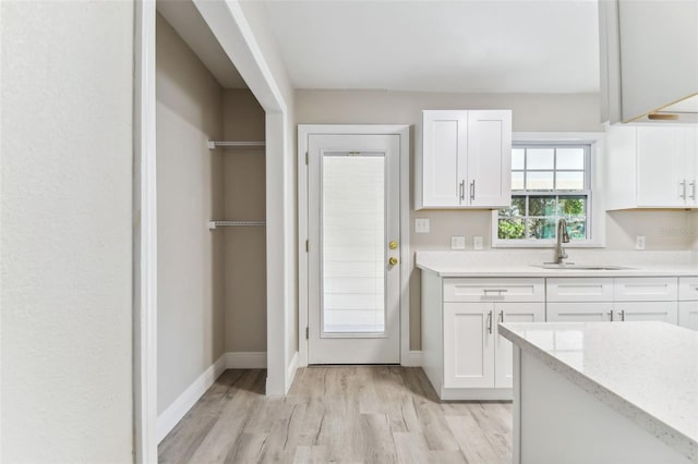 kitchen with white cabinetry, sink, light stone countertops, and light wood-type flooring