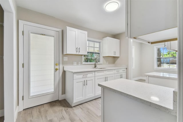 kitchen with plenty of natural light, white cabinetry, sink, and light hardwood / wood-style flooring