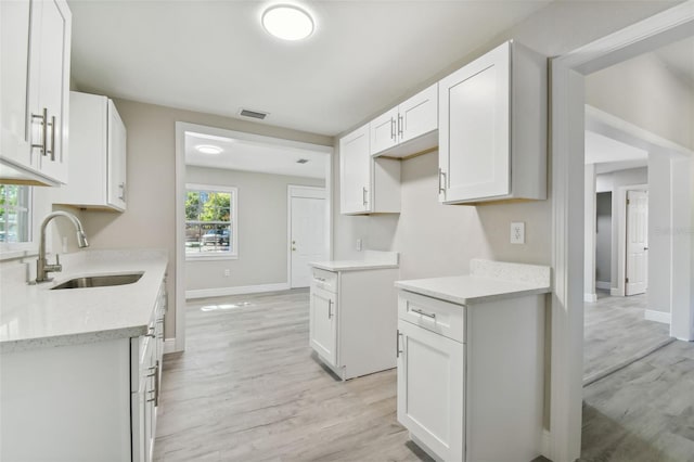 kitchen featuring light stone counters, sink, white cabinets, and light hardwood / wood-style flooring