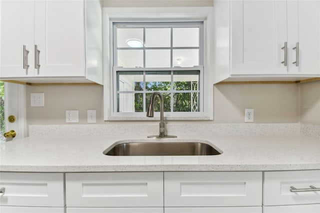 kitchen featuring white cabinets, light stone countertops, and sink