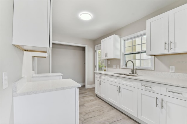 kitchen featuring light stone countertops, light hardwood / wood-style floors, white cabinetry, and sink