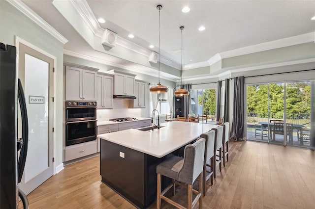 kitchen featuring a breakfast bar area, gray cabinetry, hanging light fixtures, stainless steel appliances, and a center island with sink