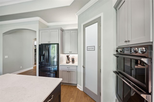 kitchen with stainless steel refrigerator with ice dispenser, double wall oven, crown molding, and light wood-type flooring