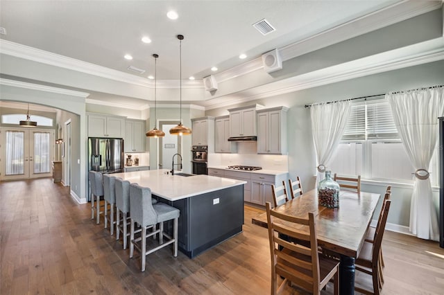 kitchen with sink, gray cabinetry, a center island with sink, pendant lighting, and stainless steel appliances