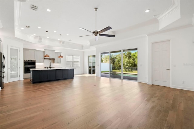 34 Concord Dr, Dunedin, FL 34698 - unfurnished living room featuring a tray ceiling, a sink, ornamental molding, a ceiling fan, and wood finished floors