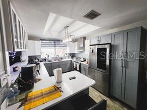 kitchen featuring appliances with stainless steel finishes, gray cabinets, hanging light fixtures, and wall chimney exhaust hood